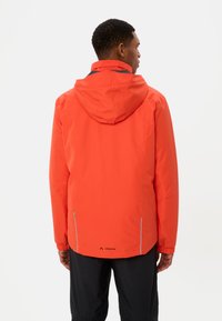 Giacca impermeabile rossa con cappuccio, polsini regolabili e dettagli riflettenti. La vista da dietro mostra una vestibilità comoda e il logo del marchio vicino all'orlo.