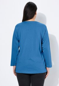 Blaues Langarm-T-Shirt mit Rundhalsausschnitt und lockerem Schnitt, gefertigt aus einem weichen, leichten Stoff mit glatter Textur.