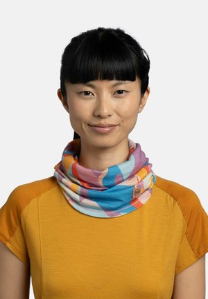 Mujer con cabello negro y flequillo que lleva un cubrecuello estampado multicolor y una camiseta de manga corta de color mostaza, sonriendo ligeramente.