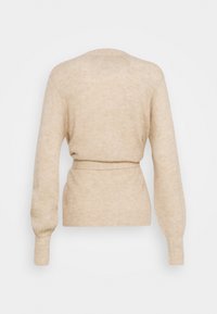 Beige stickad tröja med bälte i midjan, långa ballongsärmar och en mjuk textur. Har en rund halsringning och ribbad mudd.