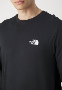 Black long-sleeve T-shirt made from smooth fabric, featuring a white logo on the left chest. Round neckline, fitted shape.