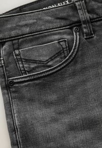 Close-up af mørkegrå denimjeans, der viser forlomme, møntlomme med nitter, bæltestrop og subtil stofstruktur.