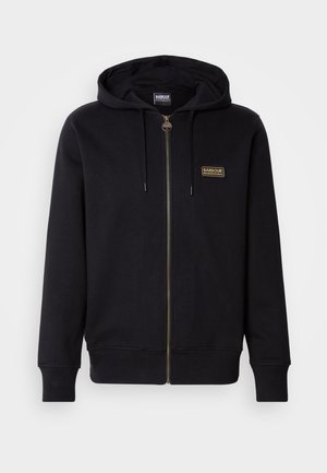 Czarna bluza z kapturem na zamek, wykonana z miękkiego materiału, z złotą łatką z logo, kieszenią na sznurku oraz ściągaczami przy rękawach i u dołu.