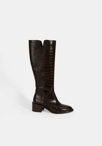 Bruine leren kniehoge laarzen met een krokodillen-embossed textuur, V-vormige opening aan de bovenkant en een chunky hak. Glad afgewerkt en robuust ontwerp.