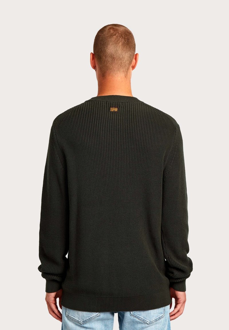 Pull vert foncé tricoté avec une texture côtelée, manches longues et col rond. Présente une petite étiquette de marque au dos.