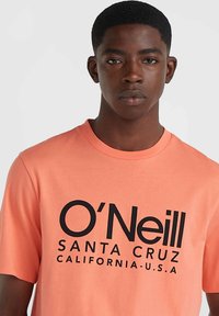 Tričko Coral O'Neill s čiernym potlačou loga, na ktorom je text "SANTA CRUZ" a "CALIFORNIA-U.S.A." na prednej strane; krátke rukávy, okrúhly výstrih.