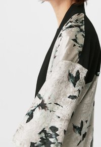 Czarna kimono z kwiatowym wzorem i szerokimi rękawami. Wykonana z teksturowanej, jasnoszarej tkaniny z zielonymi i purpurowymi kwiatowymi wzorami z przodu.