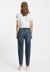 Donkerblauwe denim jeans met een relaxte pasvorm, voorzien van twee achterzakken en een gemerkte tailleband. Gecombineerd met een eenvoudig wit T-shirt en sneakers.