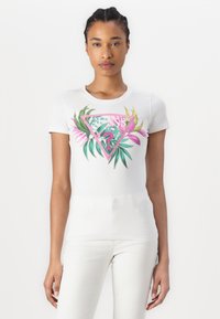 T-shirt blanc à manches courtes avec un graphique triangulaire coloré, des feuilles tropicales et du texte. Tissu en coton doux. Design simple et ajusté.