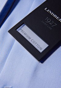 Lichtblauw gestreept overhemd van premium katoen, met een zwart label met "LINDENBERG 1927 SHIRT LINE" en "PREMIUM COTTON" label.