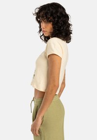 Cream-colored cropped t-shirt with short sleeves, featuring green text. Paired with light olive green drawstring pants. Soft cotton texture.