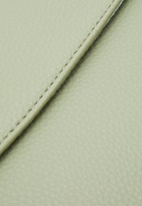 Primo piano di pelle verde chiaro con trama e cuciture visibili lungo una cucitura.