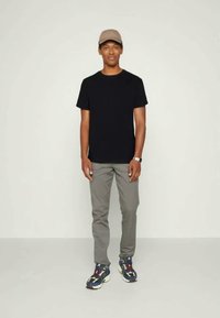 Čierne tričko, šedé nohavice a viacfarebné tenisky, doplnené béžovou čiapkou. Strih je rovný a dizajn je neformálny s viditeľnými švami.