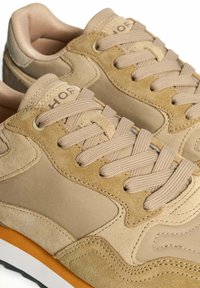 Zapatillas beige con parte superior de ante y tela, cordones planos, collar acolchado y suela de goma naranja. Presentan una textura suave y costuras sutiles.