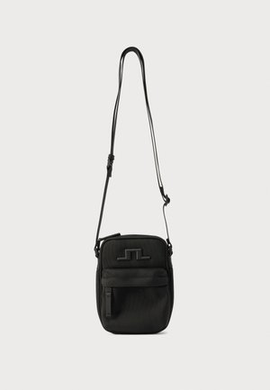 Musta olan ristiin kannettava laukku, jossa säädettävä hihna, edessä vetoketjutasku ja kohokuvioitu logo yksivärisellä taustalla.