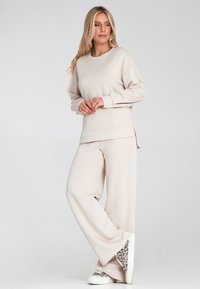 Beżowa bluza z opadającymi ramionami i bocznymi rozcięciami, w zestawie z szerokimi spodniami. Sneakersy w motyw panterki.