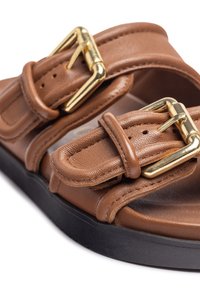 Brown leather sandals feature two wide, adjustable straps with gold-tone buckles, a padded insole, and a black outsole.