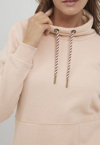 Felpa con cappuccio rosa chiaro dalla texture morbida, con un laccio di chiusura con dettagli dorati e una tasca frontale.