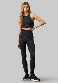 Set sportivo nero composto da un top corto con scollatura rotonda e leggings a vita alta. Tessuto testurizzato con padrões discreti, abbinato a sneakers nere.