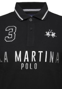 Sort polo shirt lavet af bomuld, med en gråstribet krave, broderet nummer "3" og sølv "LA MARTINA POLO" tekst.