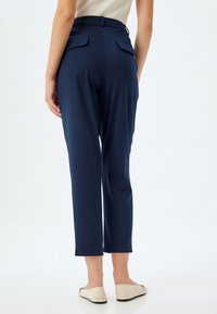 Navyblauwe op maat gemaakte broek met een gladde textuur, korte lengte en twee achterzakken. Gestoeld met platte, lichtgekleurde schoenen.