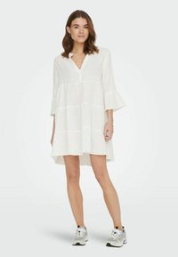 Weißes, knielanges Kleid aus leichtem Stoff, mit einem Knopfverschluss am Ausschnitt, ausgestellten Ärmeln und horizontal gestreifter Textur.