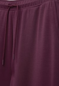 Bordowe spodnie dresowe wykonane z miękkiego materiału, z elastycznym pasem i sznurkiem oraz praktycznymi bocznymi kieszeniami. Gładka faktura.