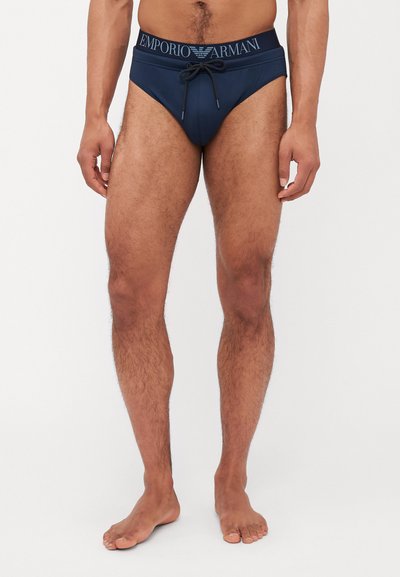 Sötétkék úszóalsó az Emporio Armani-tól, zsinóros derékkal és logós derékpánttal, sima, rugalmas anyagból készült.