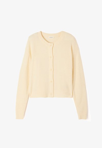 Cardigan court beige clair en tricot doux, avec un col rond, une fermeture à boutons, et des poignets et un ourlet côtelés.