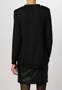 Czarna bluzka z długim rękawem o luźnym kroju, z okrągłym dekoltem i mankietami na guziki, zestawiona z czarną skórzaną spódnicą.