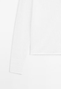 Witte lange mouw trui, gebreide stof, ribbelstructuur en een cropped ontwerp. Randen zijn iets rafelig, met een zachte, lichte uitstraling.