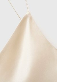 Camicetta in satin di un colore beige chiaro con spalline sottili e una texture liscia e lucida. Presenta un design con scollo triangolare.