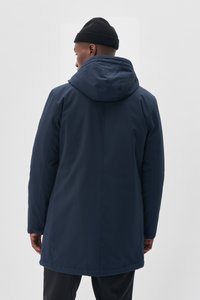 Chaqueta con capucha de color azul oscuro, con un exterior suave y resistente al agua, que presenta un corte recto y puños ajustables. Diseño sencillo, sin patrones visibles.