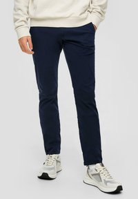 Navyblauwe stretchbroek met een slanke pasvorm, gemaakt van zachte katoenen stof. Beschikt over zijzakken en een strakke uitstraling. Gecombineerd met lichte sportschoenen.