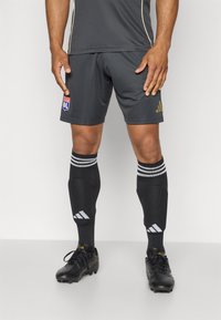 Shorts de sport noirs avec le logo doré d'Adidas et le blason du club de Lyon. Chaussettes noires avec des rayures blanches ; chaussures de football noires avec lacets.