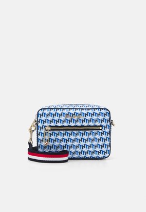 Blå mønstret skuldertaske med geometriske former, gulddetaljer, en lynlåslomme og en stribet stofrem i rød, hvid og marineblå.