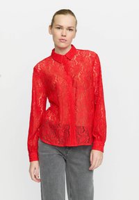 Red lace blouse with a collared neckline, button front, and long sleeves. Features floral patterns and a semi-sheer texture.