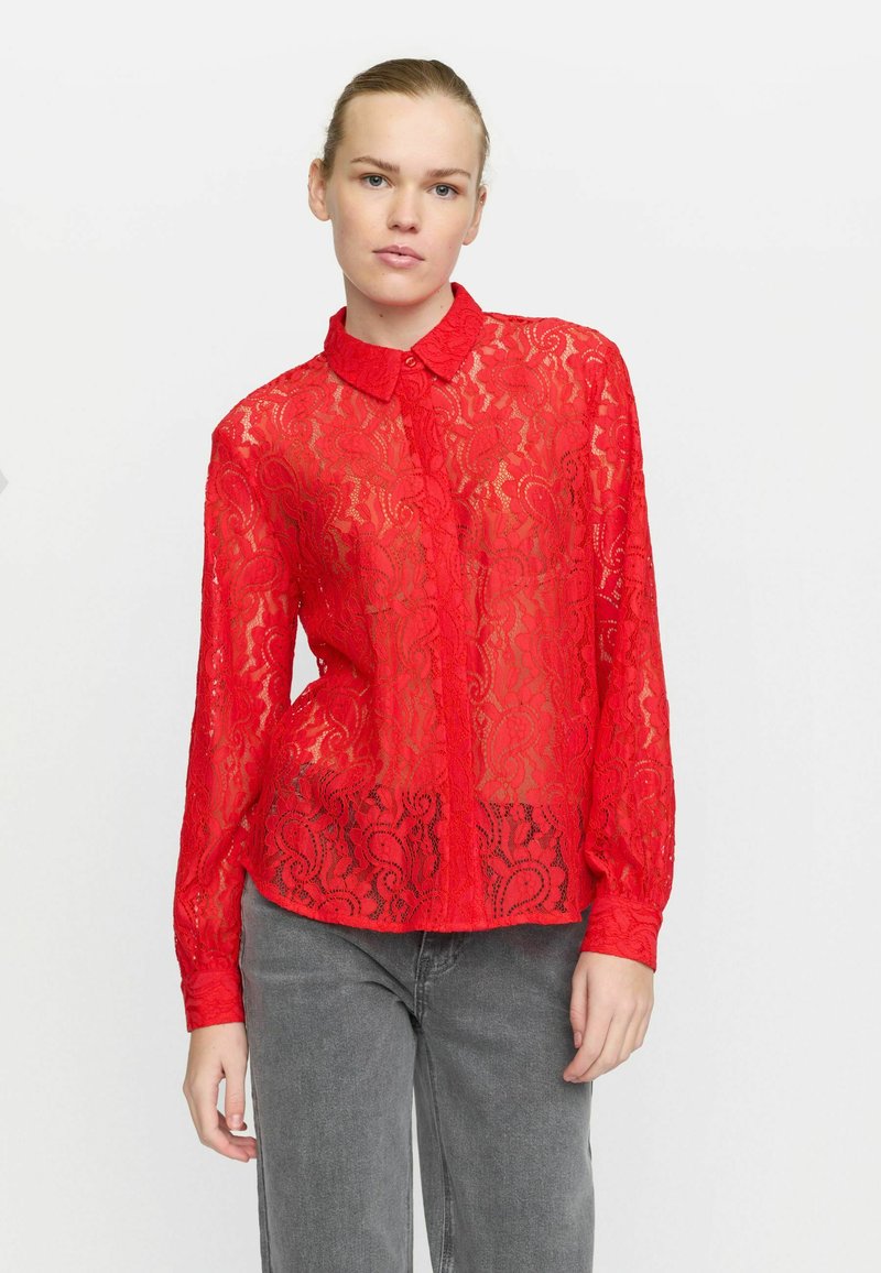 Red lace blouse with a collared neckline, button front, and long sleeves. Features floral patterns and a semi-sheer texture.