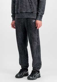 Pantalons de jogging en polaire gris foncé avec des poignets élastiques, des poches avant et une finition texturée, associés à des chaussures de sport noires avec des accents argentés.