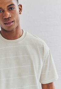 Light beige short-sleeve t-shirt featuring horizontal white stripes, a round neckline, and a soft texture, worn by a man.