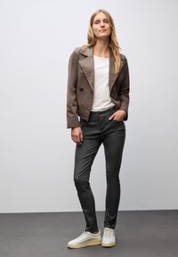 Brun dubbelknäppt jacka över en vit skjorta, parat med mörkgrå slim-fit byxor och vita sneakers. Släta texturer och skräddarsydd passform.