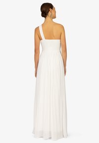 Ein schulterfreies weißes Kleid mit einem gerafften Oberteil und einem fließenden, plissierten Rock, das leichtes, luftiges Material und ein minimalistisches Design hervorhebt.