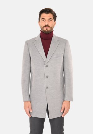 Cappotto in lana grigio chiaro con una vestibilità sartoriale, dotato di rever a punta, tre bottoni e una tasca sul petto, indossato sopra un dolcevita bordeaux.
