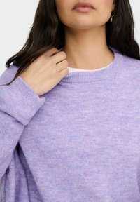 Pull en maille violet avec un col rond côtelé et une coupe décontractée. Le tissu semble doux avec une texture légèrement chinée et des manches longues.