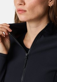 Svart ribbad zip-up jacka med hög krage. Har en kraftig dragkedja och en figurnära design. Slät tygstruktur framhävd.