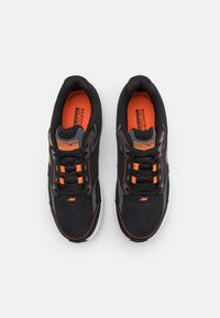 Zapatillas deportivas negras con material de malla, acentos naranjas, suela acolchada y seis cordones negros. Presenta la marca 'SKECHERS GO RUN'.