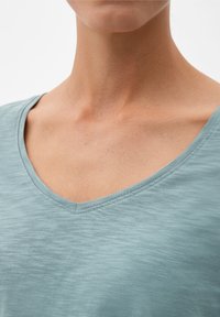 Helles blaues V-Ausschnitt-T-Shirt aus weichem, strukturiertem Stoff. Verfügt über einen sauberen Halsausschnitt und subtile Stickdetails, die ein lässiges Design unterstreichen.