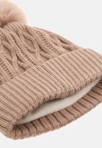 Beige Strickmütze mit strukturiertem Zopfmuster, ausgestattet mit einem flauschigen Pompon oben und einem weichen Innenfutter.