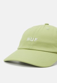 Light green cotton cap featuring a curved brim and embroidered "HUF" logo in white. Designed with ventilation holes and stitching details.