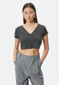Grå kortærmet t-shirt med V-hals, lavet af blødt stof. Båret med højtaljede grå bukser med knapdetalje.